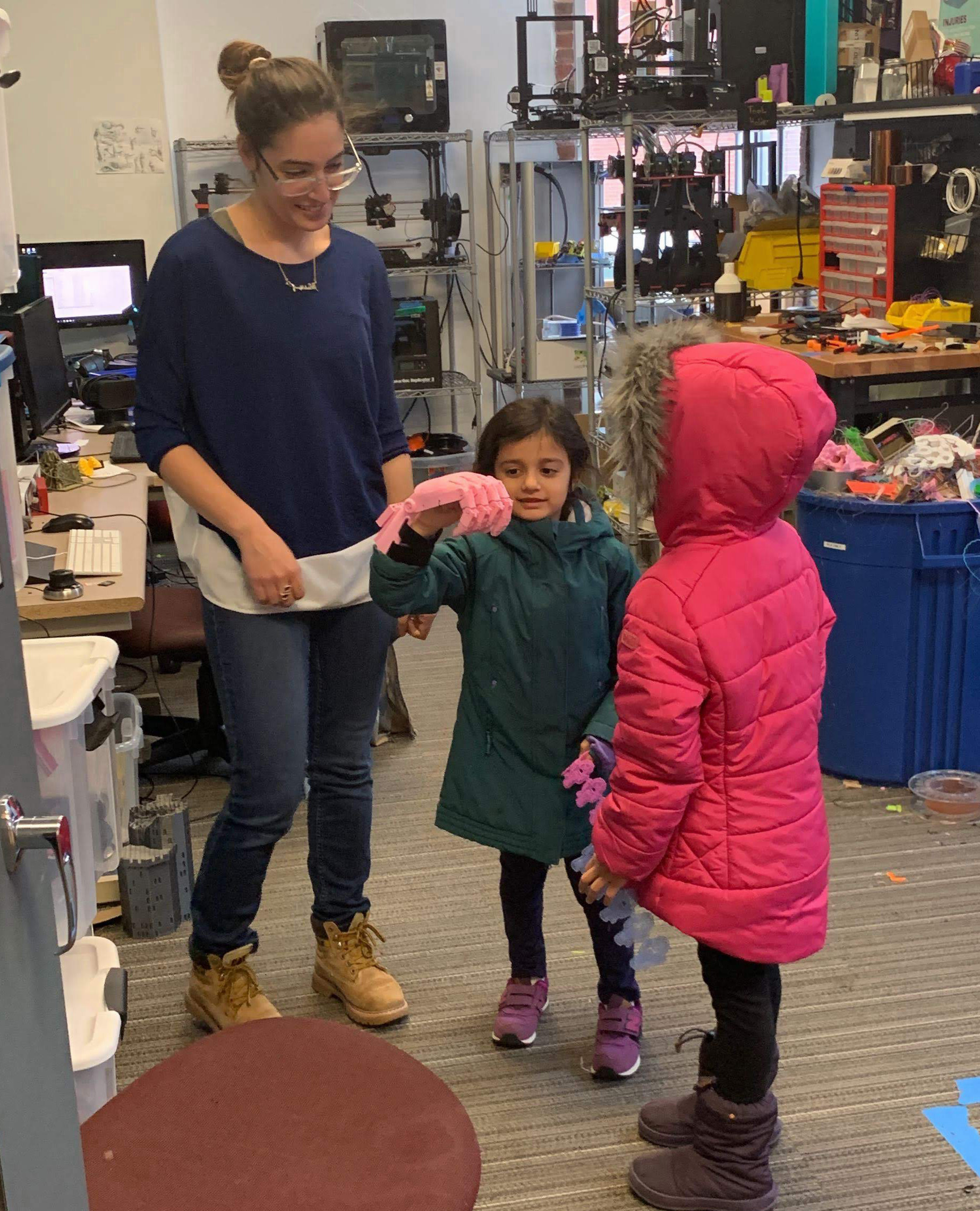 A teacher assisting children in trying out E-Nable 3D printed prosthesis