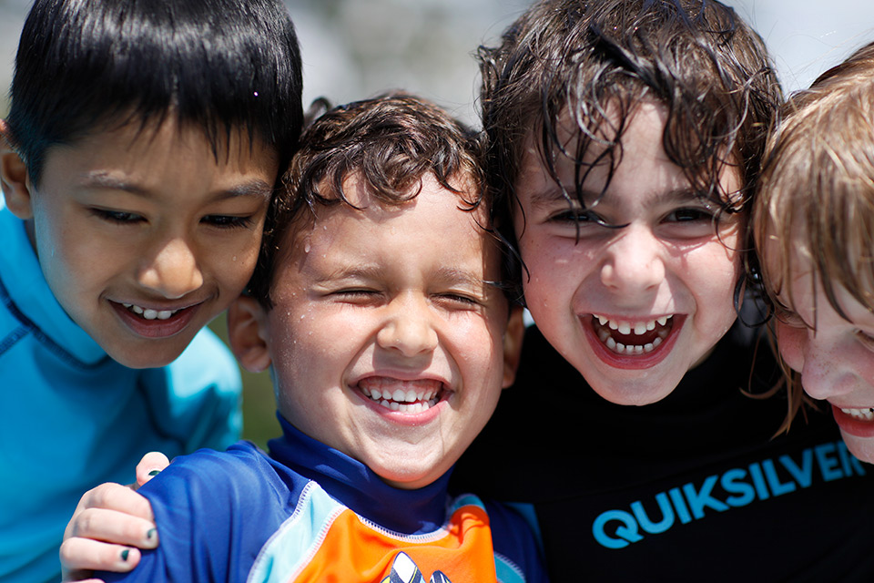 Four children with wet hair smile while playing in the water