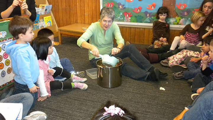 A teacher pouring something into a pot with children observing